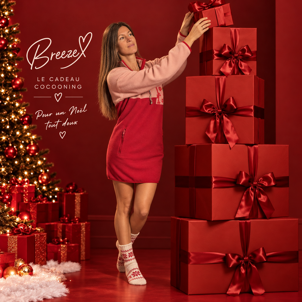 Femme portant la robe polaire Peek Breeze rose et rouge à demi-zip, déposant un cadeau sur une pile de boîtes rouges près d'un sapin de Noël