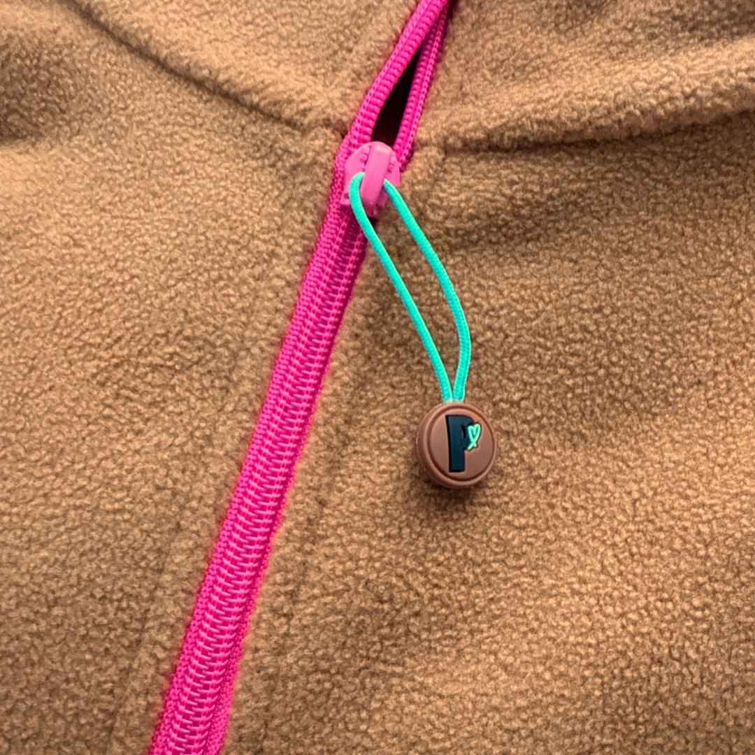 Gros plan du zipper fuchsia et de la tirette turquoise du polar court Toffee Peek Breeze