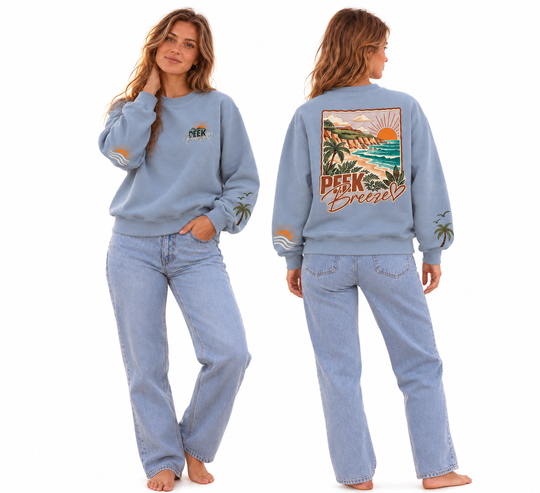 Femme portant le Crewneck Coastal bleu pâle Peek Breeze, chandail en coton ouaté composé de 76 % coton et 24 % polyester, présenté de face et de dos avec logo poitrine, illustrations sur les manches et grand imprimé tropical au dos représentant une plage, des palmiers et un coucher de soleil.
