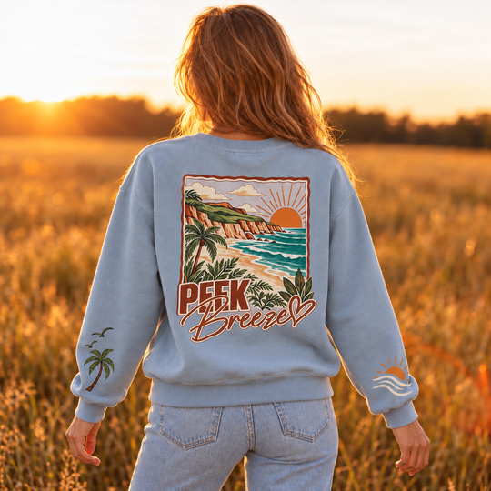 Vue de dos du Crewneck Coastal bleu Peek Breeze, chandail confortable pour femme avec grand imprimé de paysage côtier, palmiers et soleil.