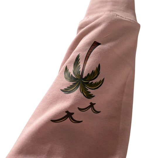 Gros plan de la manche du Crewneck Coastal rose pâle Peek Breeze montrant un imprimé de palmier et d’oiseaux sur le coton ouaté.