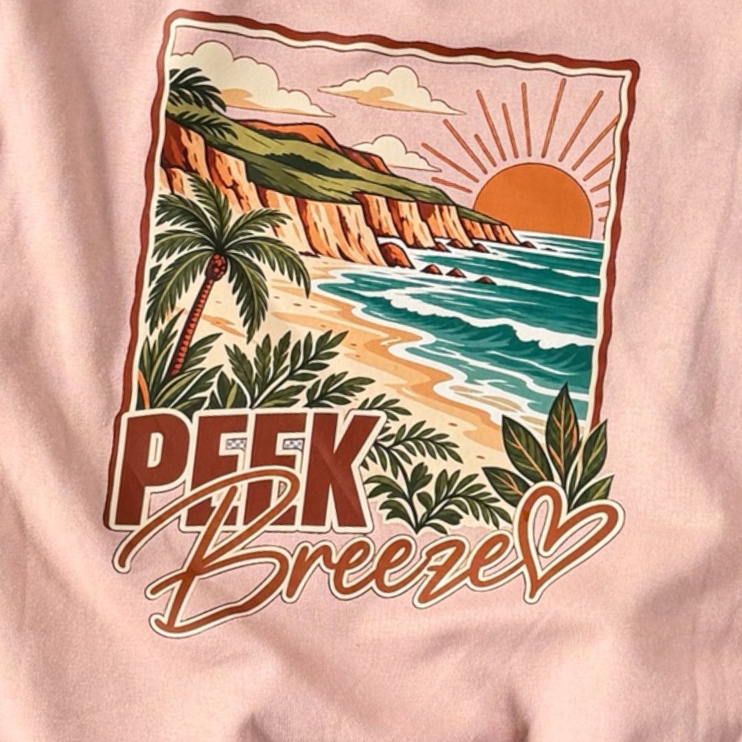 Détail du grand imprimé au dos du Crewneck Coastal rose pâle Peek Breeze représentant une plage tropicale, des palmiers, l’océan et le logo de la marque.