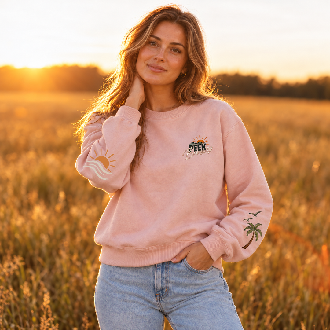 Femme portant le Crewneck Coastal rose pâle Peek Breeze, chandail en coton ouaté confortable avec logo poitrine, dans un paysage naturel au coucher du soleil.