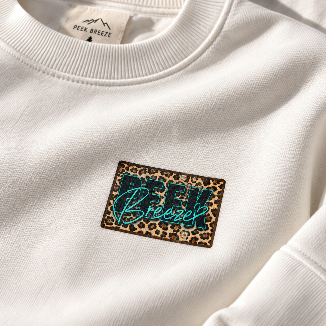 Détail du logo Peek Breeze imprimé motif léopard sur le crewneck WILD blanc