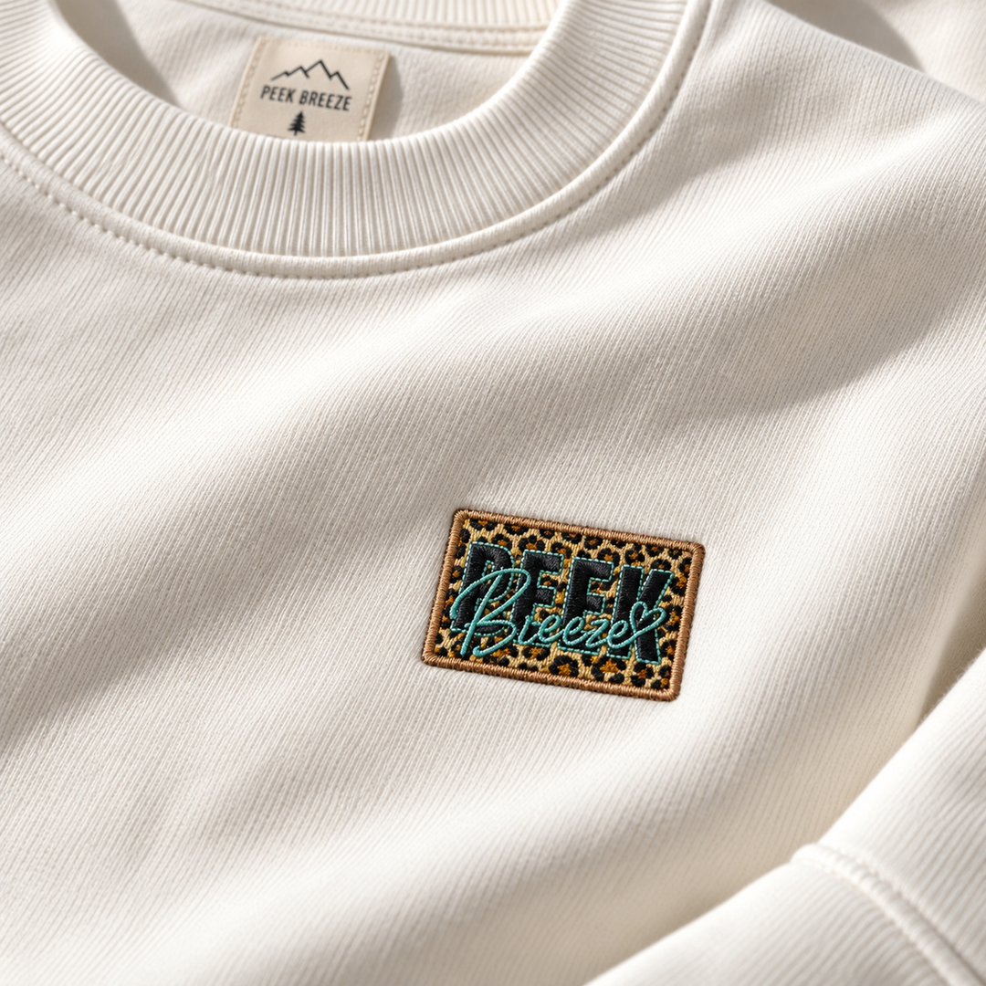 Détail du logo Peek Breeze brodé motif léopard sur le crewneck WILD blanc