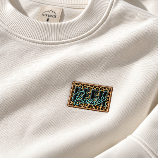 Détail du logo Peek Breeze brodé motif léopard sur le crewneck WILD blanc