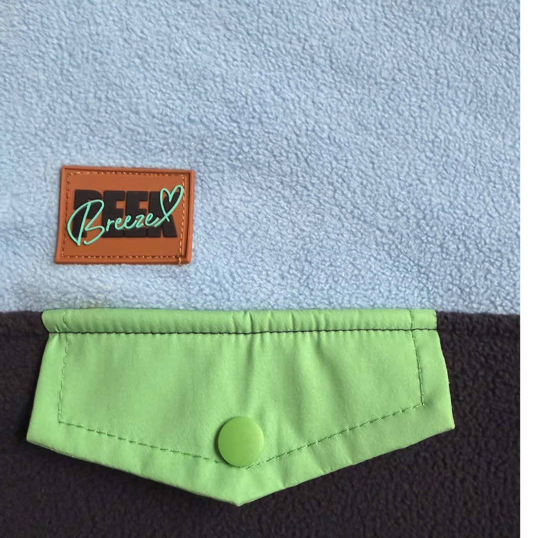 Détail de la poche poitrine vert lime à bouton-pression et de l’étiquette Peek Breeze sur la robe polaire Seaside bleu pâle et marine.
